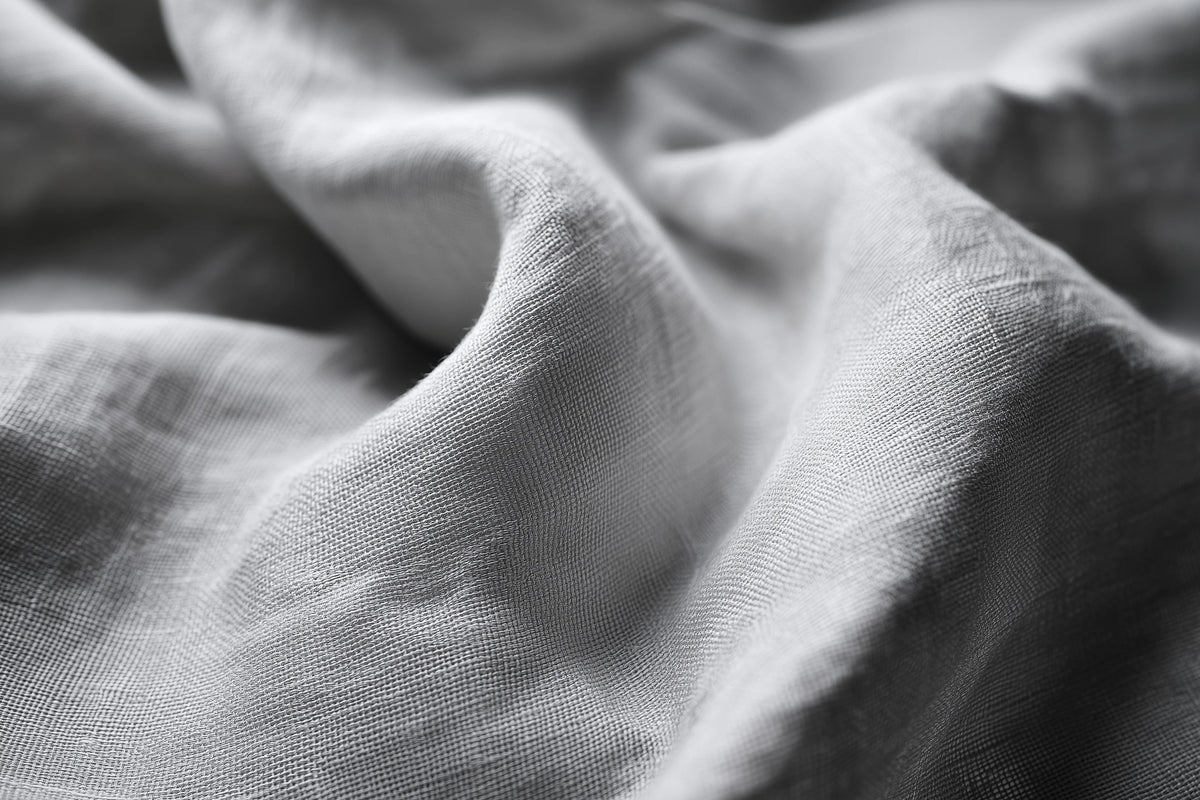 Close-up of draped light gray fabric with soft folds and visible woven texture.