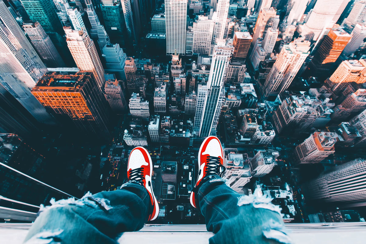 Person wearing red and white air jordans, sitting on the edge of a skyscraper looking down on the New York city below.