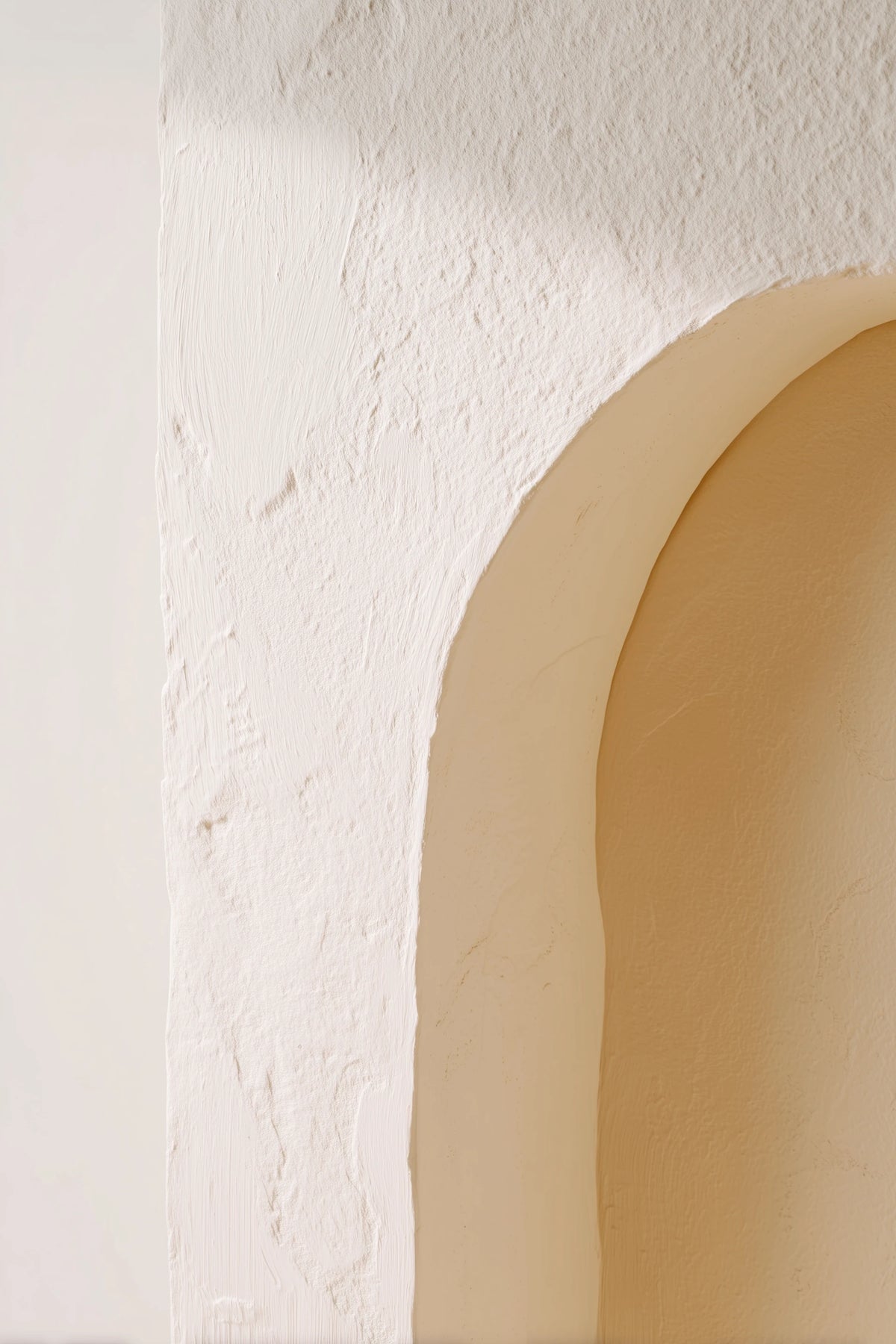A close-up architectural detail of a textured off-white plaster wall with a warm beige arched recess.