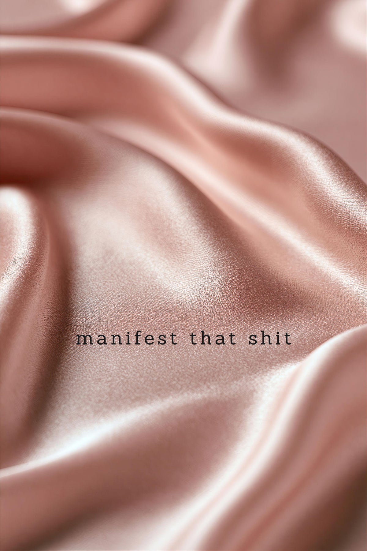 A close-up of draped satin fabric in a soft blush pink color, with the text 'manifest that shit' printed in a small black serif font near the center.