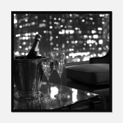 Black framed wall art of two champagne glasses and a bottle in an ice bucket on a table with a cityscape in the background.