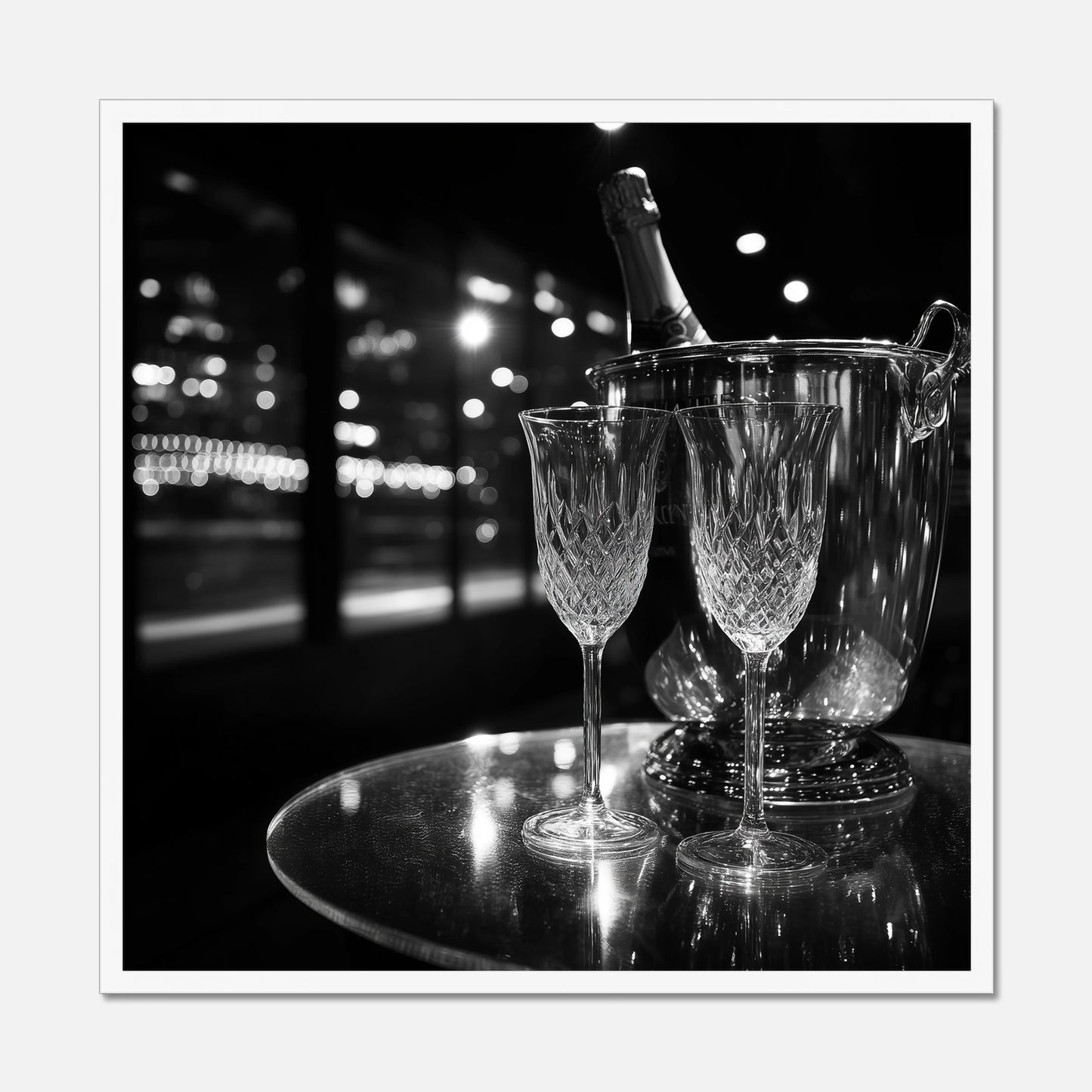 White framed print of two wine glasses and a bottle of champagne in an ice bucket on a reflective surface with a night-time cityscape background.