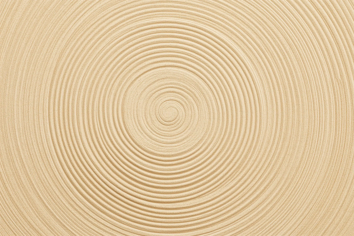 A close-up of a light beige sand textured surface with concentric circular grooves radiating from the center.