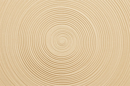 A close-up of a light beige sand textured surface with concentric circular grooves radiating from the center.