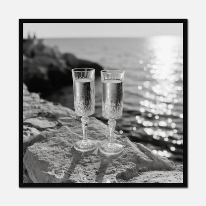 Two champagne glasses on a rock by the water displayed in a black wooden frame.