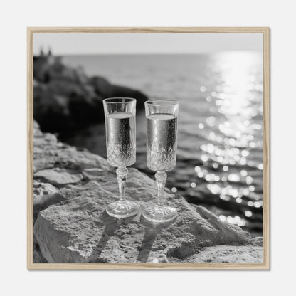 Two champagne glasses on a rock by the water displayed in a natural oak wooden frame.