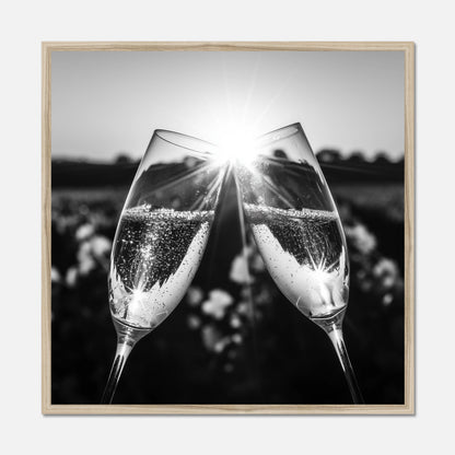 Black and white, natural oak framed wall art featuring two champagne flutes clinking together with bright sunburst and blurred outdoor background.
