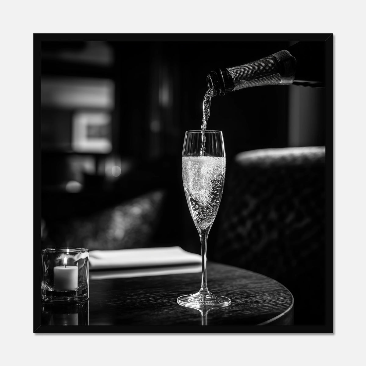 Black framed print of champagne being poured into a glass on a table with a blurred background