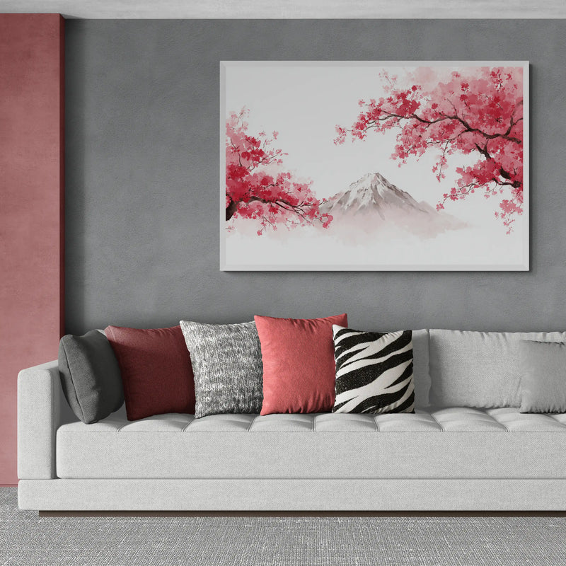 A framed wall art print featuring pink cherry blossom branches and a snow-capped mountain on a light background, displayed above a modern gray sofa with decorative throw pillows in a styled living room.