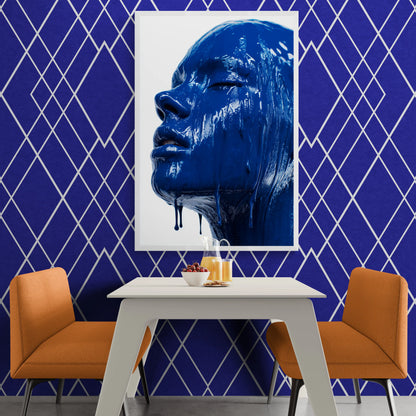 Blue abstract painting of a face on a white frame against a blue geometric-patterned wall with orange chairs and a white table.