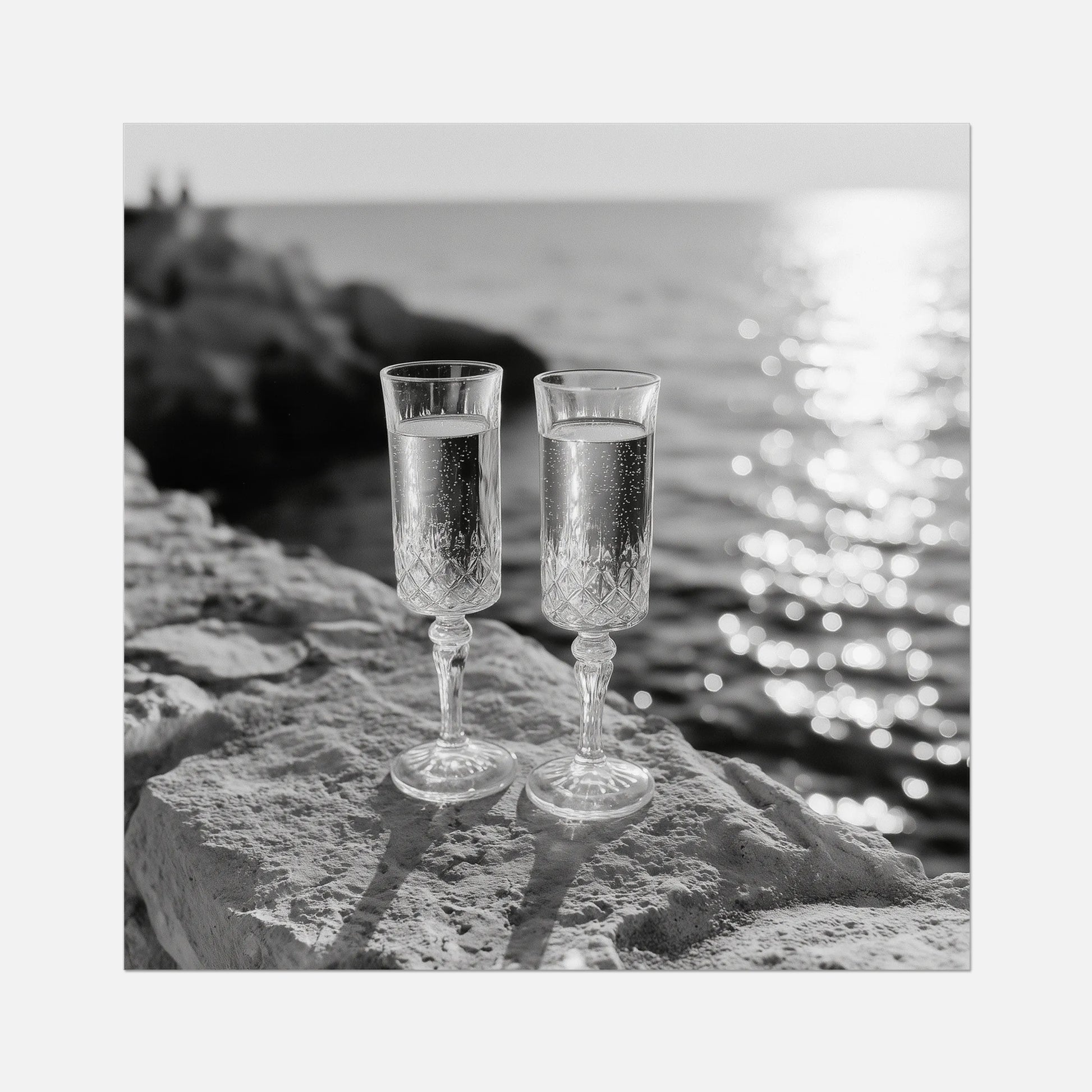 Two champagne glasses on a rock by the water with a wooden frame.
