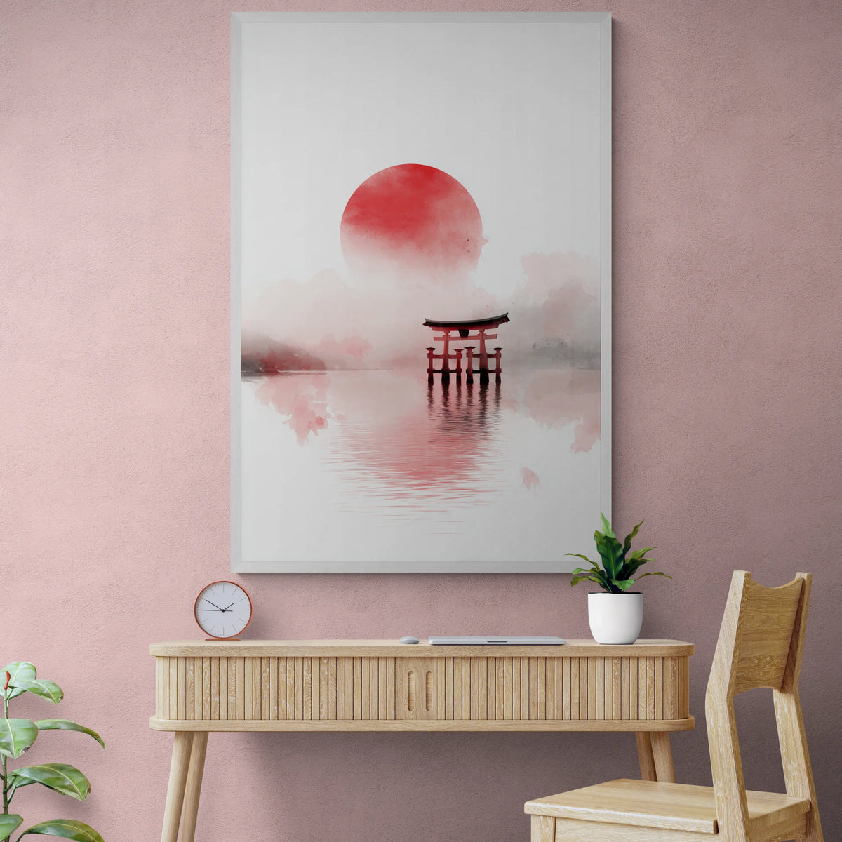 A vertical framed wall art print featuring a red sun and torii gate in misty water, displayed on a pink wall above a light wood console table with a plant and chair.