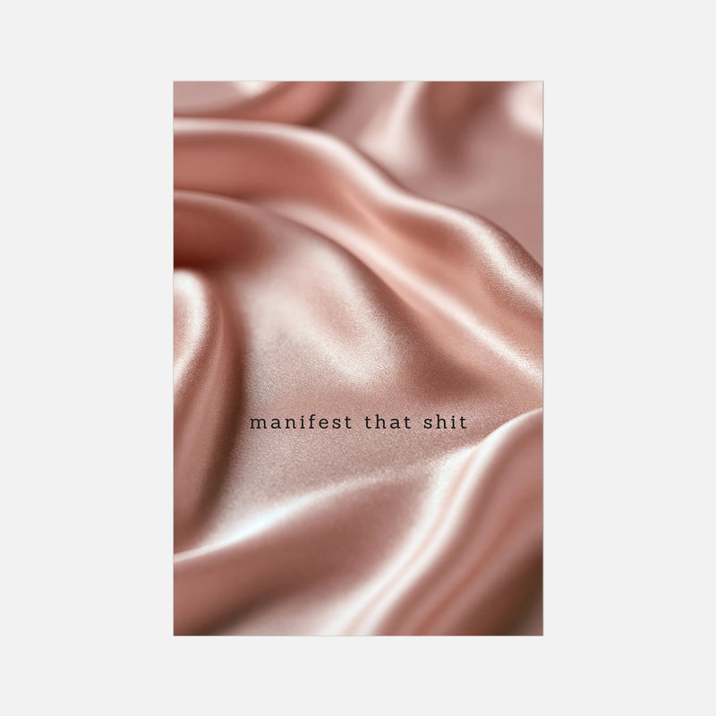 A rectangular art print featuring a close-up photograph of draped, shiny pink satin fabric with the text 'manifest that shit' printed in small black lowercase letters near the center, shown against a light gray background.