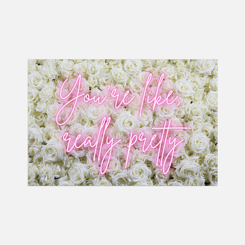 A rectangular wall art print featuring a background of dense white roses with pink cursive text reading 'You're like, really pretty' centered on a light gray backdrop.
